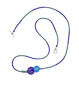 a mixed bead necklace with a turquoise and blue strand embellished with a single red bead at intervals and accented with a purple glass faceted bead ad a bright blue round bead.