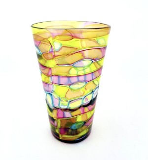 a glass tumbler cup with a complex pattern of layered, swirly bands of translusent colors from yellow to circles of green and bands of pink. 