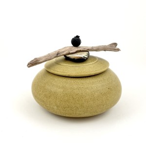 a round ochre ceramic pot with a lid embellished with a piece of driftwood and a carved black ceramic button.