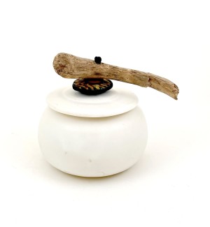 a round white ceramic pot with a lid embellished with a piece of driftwood and a carved black ceramic button.
