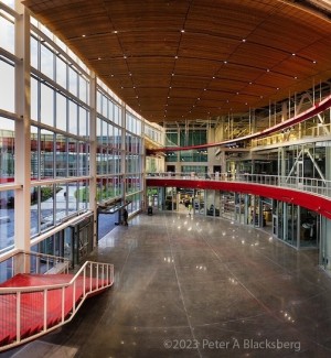 a panoramic interior view of a glass and steel clad modern building with an expansive walkway with a bright red hand rail.