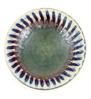 a hand thrown ceramic serving bowl with a multi colored glaze with a green center and floral petal pattern in maroon around the edge. 