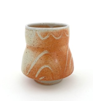 a hand thrown footed ceramic drinking cup with an hour glass shape and glaze that blends from pebbly white to a blush orange. 