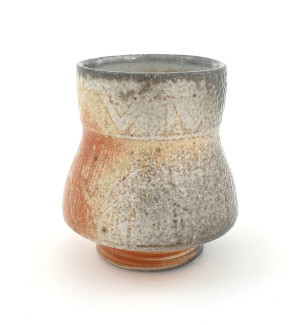 a hand thrown footed ceramic drinking cup with an hour glass shape and glaze that blends from white to orange to charcoal grey.