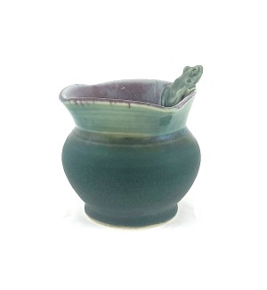 a small hand thrown rounded vase with a dark green glazed body and a light green folded rim with a green tree frog perched at the edge.