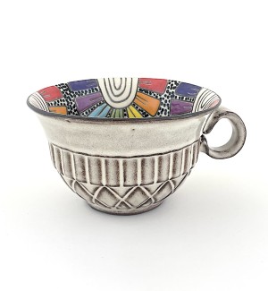 a ceramic mug in the shape of a bowl illustrated interior of a rainbow colored flower patten and a beige quilted surface exterior.