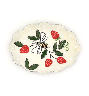 a ceramic trinket tray with a scalloped edge and an illustration of a bee amongst red strawberries.