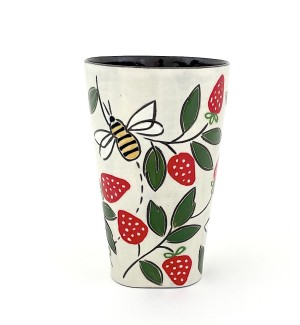 a ceramic tumbler with a white base and illustration of red strawberries, green leaves and a yellow bee.