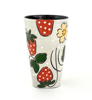 a ceramic tumbler with a white base and illustration of red strawberries, green leaves and small yellow flowers. 