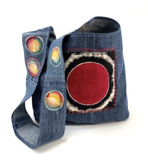 a shoulder bucket bag sewn from blue jean material and embellished with painted red and yellow circles and decorative stitching.