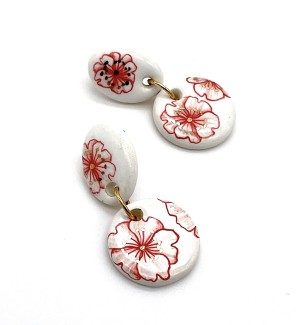 a pair of handmade white ceramic earrings comprised of an oval piece linked with a round piece both illustrated with red and gold poppies. 