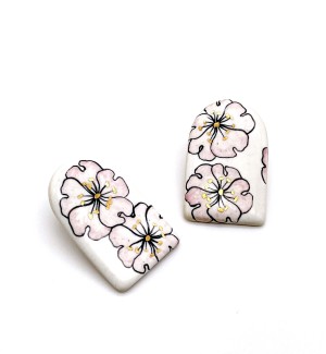 a pair of handmade white ceramic earrings in an arch shape with illustrations of pink poppies with gold details.