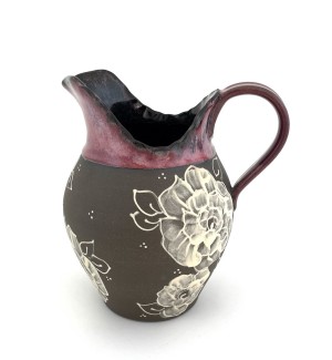 a ceramic pitcher with a handle  with a dark clay body, brush stroke illustrations of roses and a rosy glaze at the rim and handle.