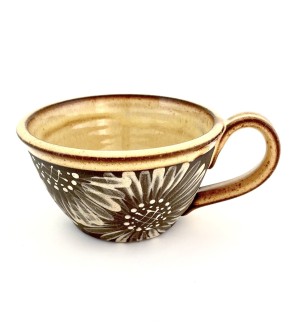 a hand thrown bowl shaped ceramic mug with a handle, a dark clay body and hand illustrated sunflower designs on the surface. 
