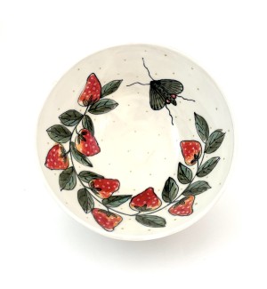 a white ceramic bowl with hand illustrated red strawberries, green leaves and a winged moth.