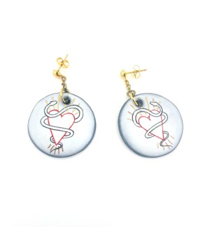 a pair of round white ceramic dangle earrings with an illustration of a heart entwined with a snake.