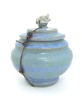 A blue ceramic lidded jar with a small sculpture of a bat on top, tied with a waxed leather cord.