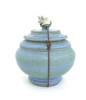 A blue ceramic lidded jar with a small sculpture of a bat on top, tied with a waxed leather cord.