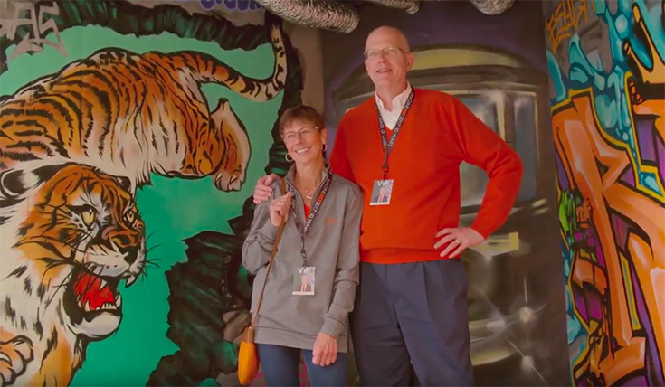 Dr. Munson and his wife standing in front of a mural painted on a wall