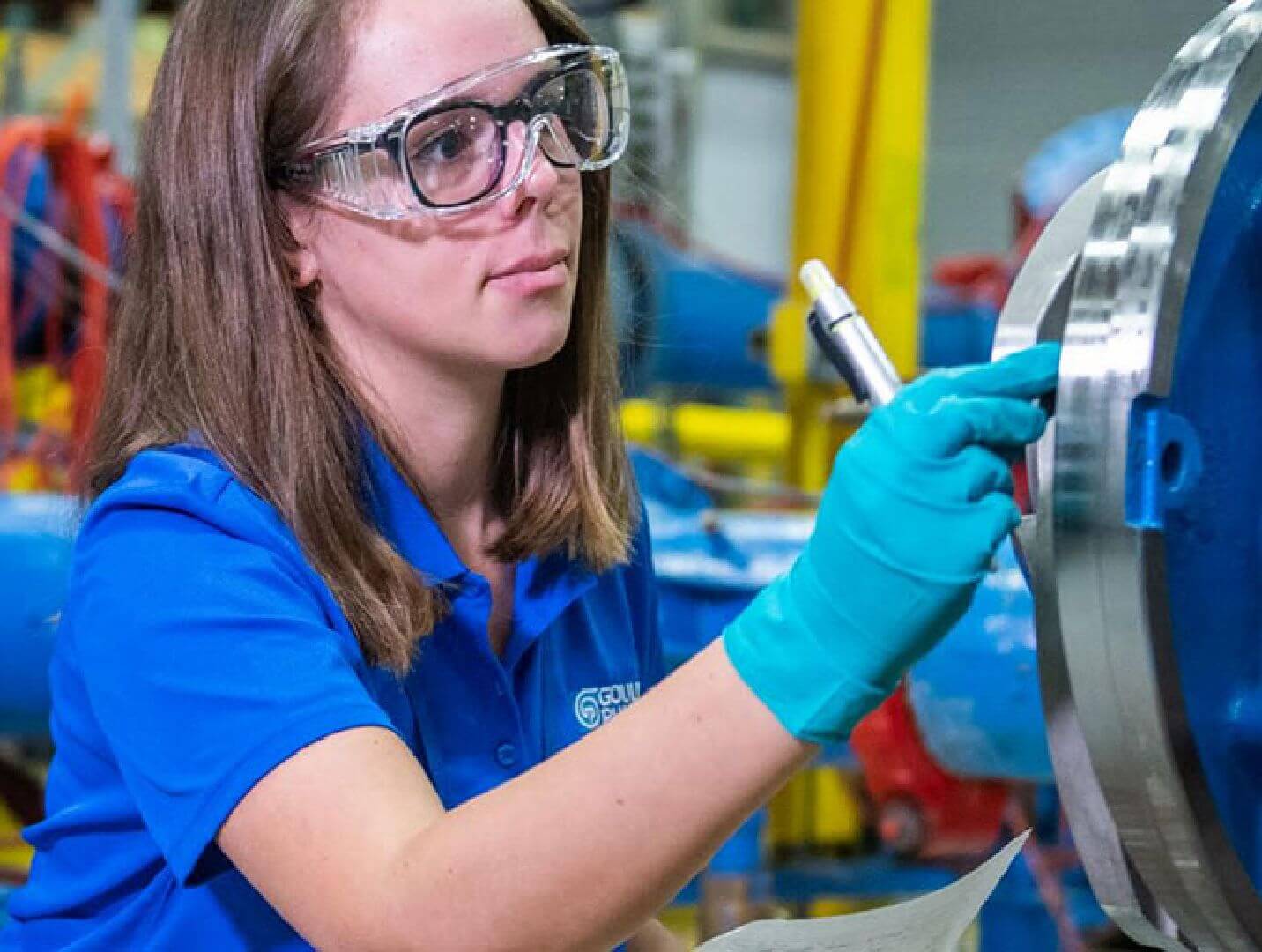 A person wearing gloves and safety glass while inspecting a piece of machinery.
