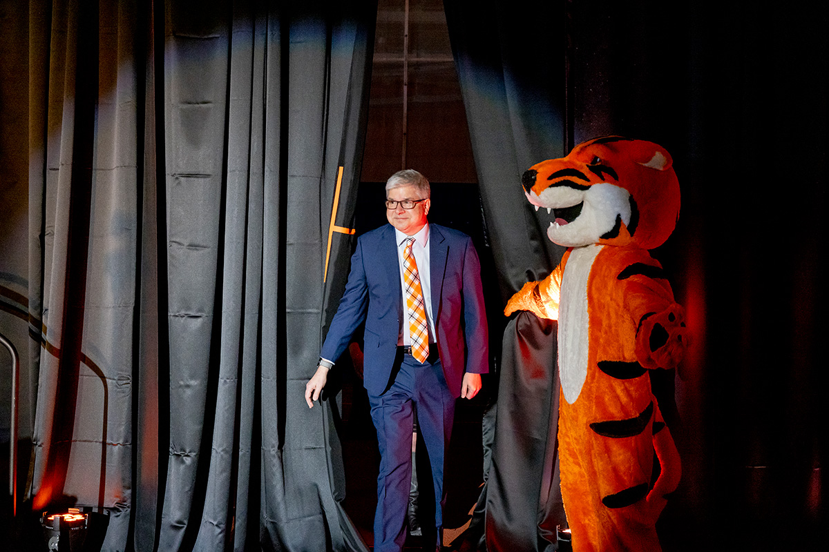 President Sanders walks through a curtain, as RITchie the RIT Tiger holds it back for him.