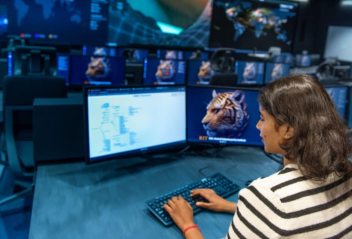 An R I T student sitting in a computer lab, working at a computer.