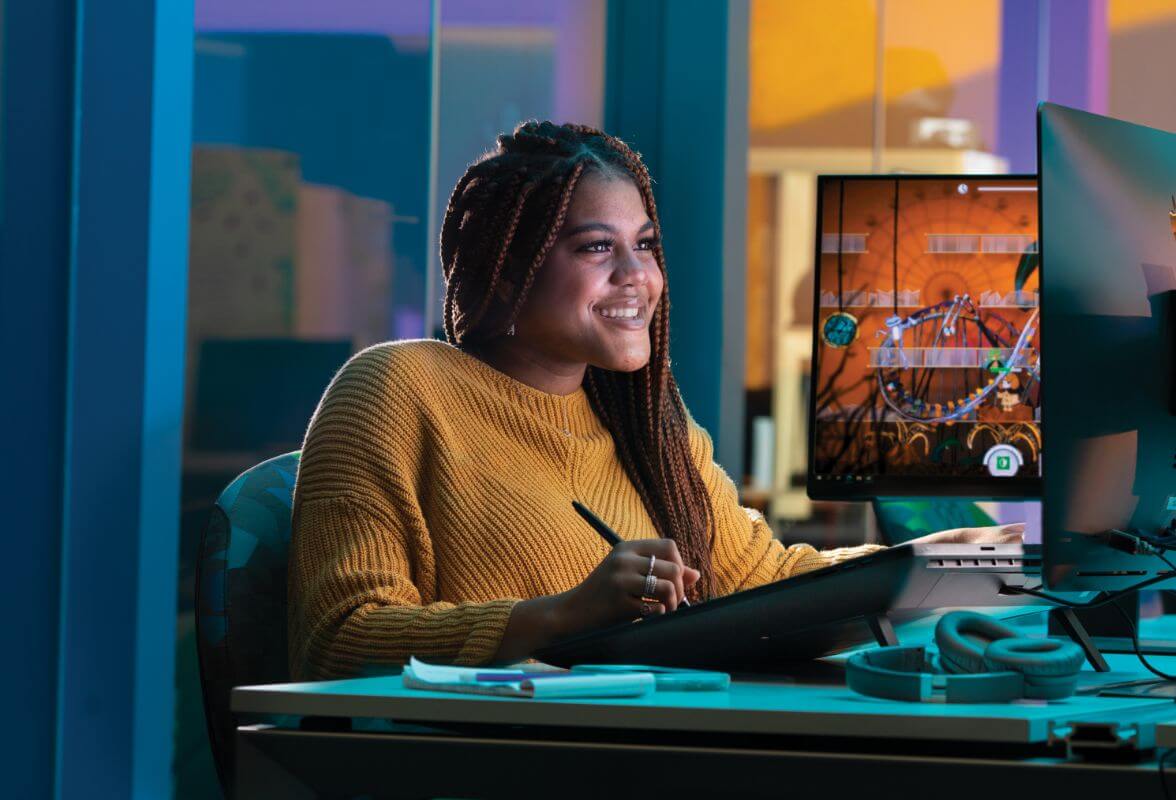 A student smiling, looking at a computer screen while sitting at a desk.