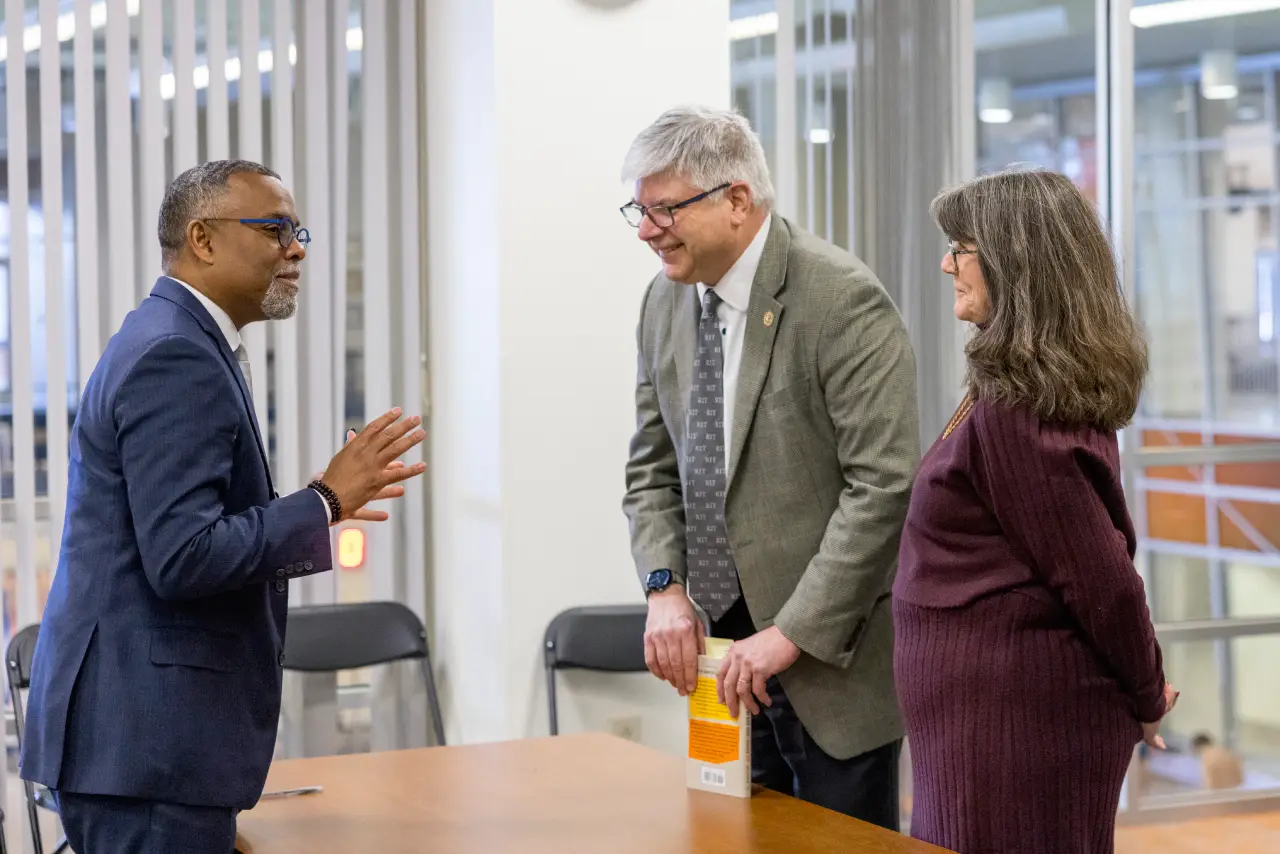Bill and Emily Sanders talking with Eddie Glaude Jr across a wooden table.
