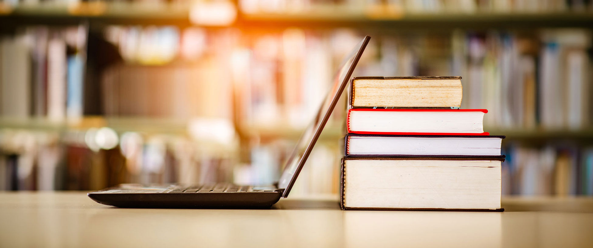An open laptop computer monitor rests against a pile of books.