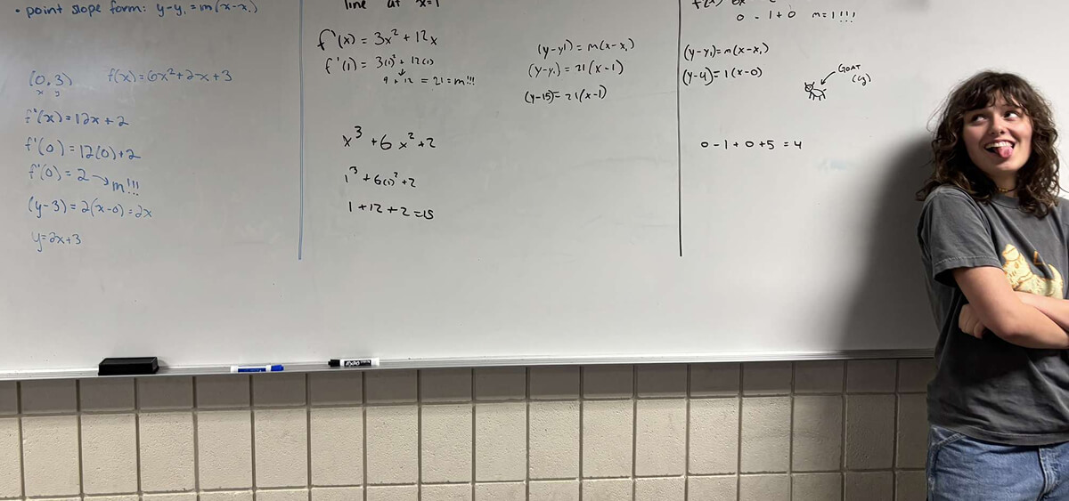 Clara-Zofia Gawlowicz standing next to a whiteboard with several equations written on it.