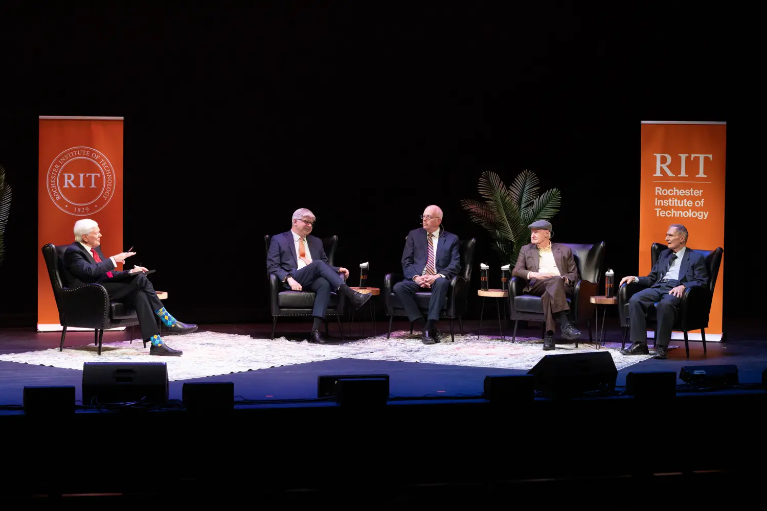 Former presidents sitting on a stage in comfortable chairs