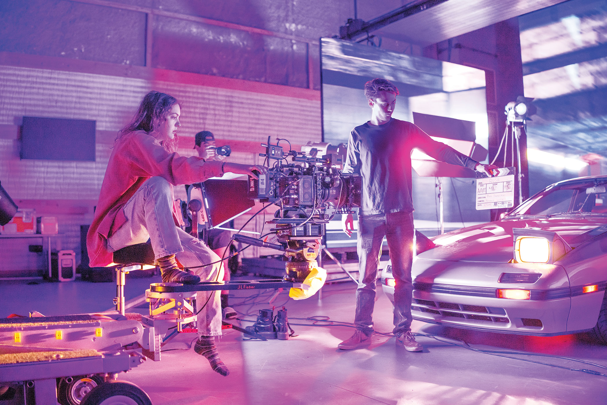 3 People working in a sound stage with a car with its lights flipped up