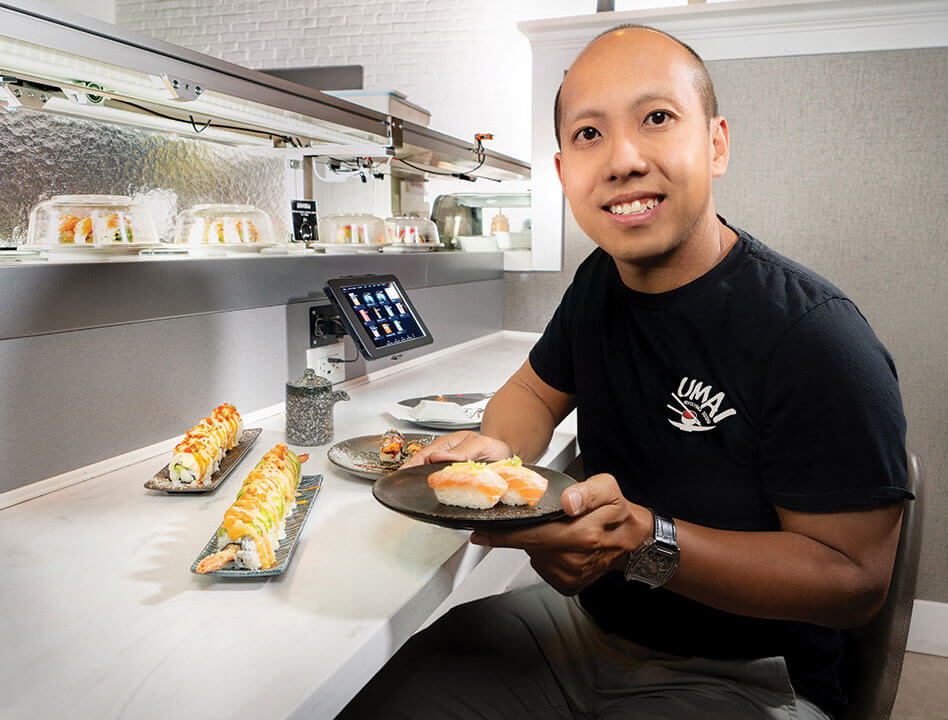 Phil Nguyen sitting in a restaurant holding a plate of sushi.