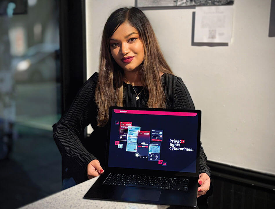 Nuzhat Minhaz sits on a table holding a laptop that is open to a screen displaying information about her company called Priva C.