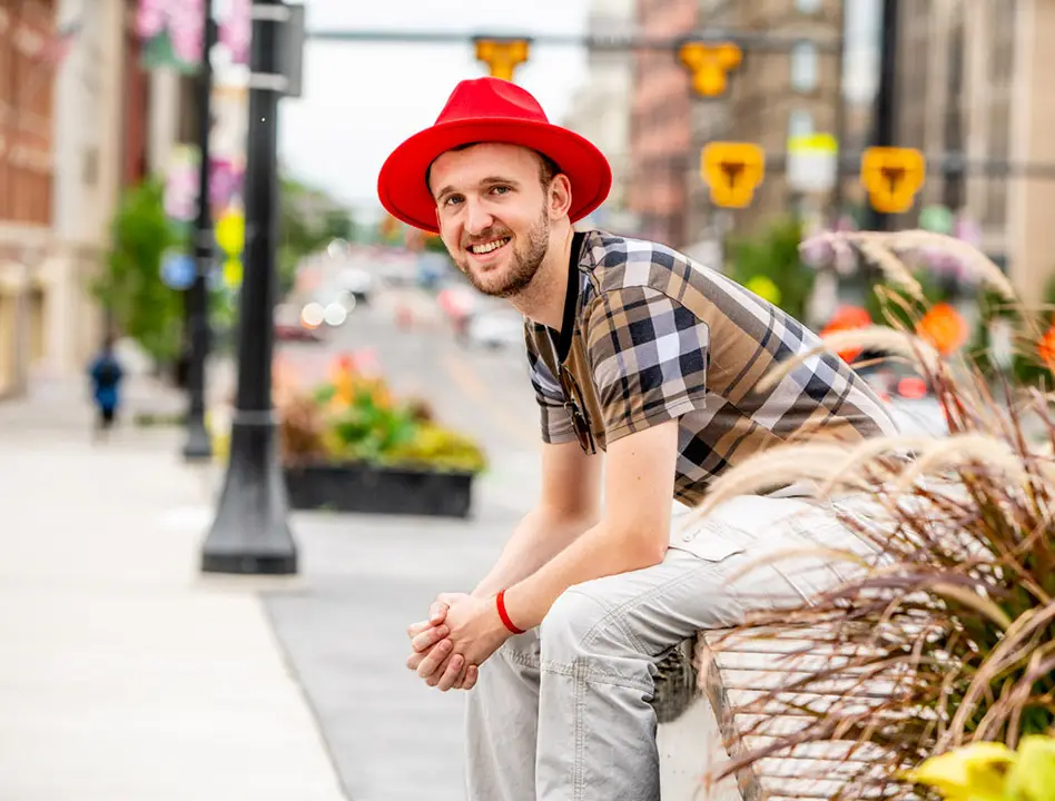 Justin W. Flory sitting on a planter wearing a bright red fedora hat