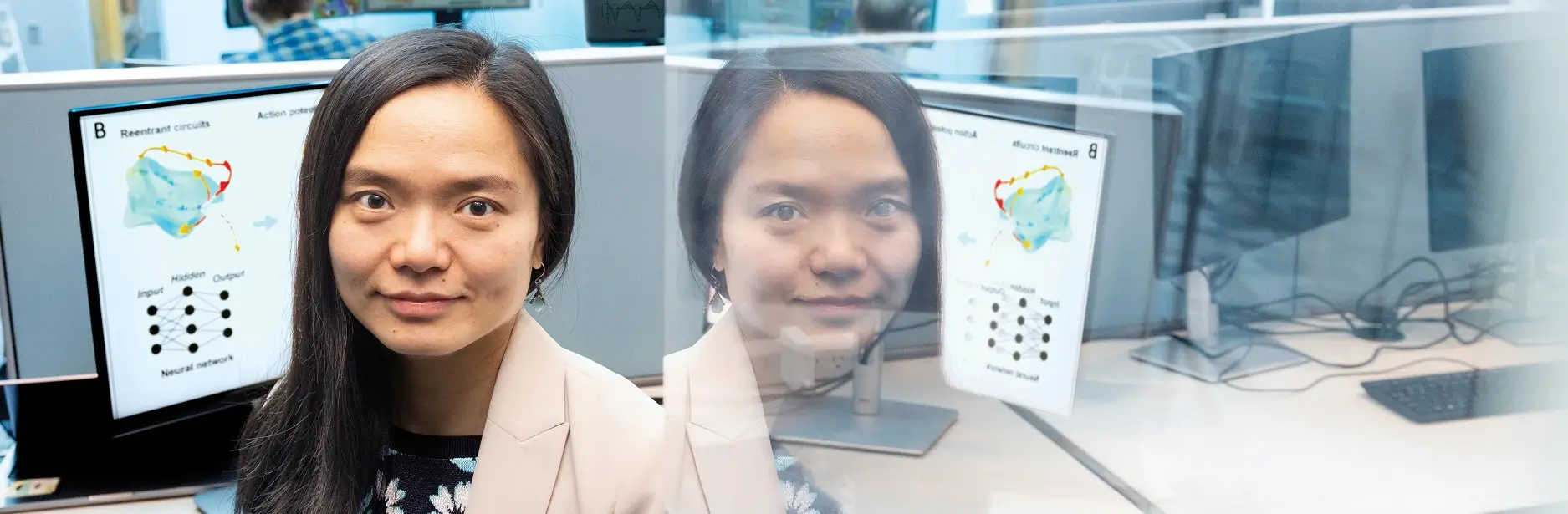 Professor Linwei Wang sitting next to a computer monitor showing a graph. Her image is reflected on the right.
