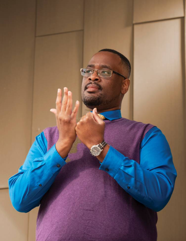 Joseph Hill wearing a blue shirt and purple sweater signing.