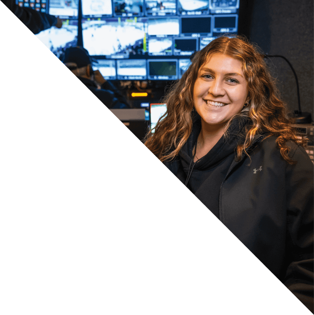 Woman smiling in front of a wall of monitors