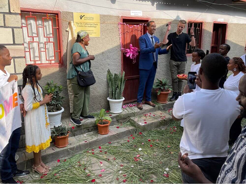 A crowd watching as a woman stands looking surprised next to two men making an announcement in front of a building in Ethiopia.