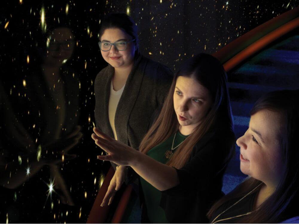 Jeyhan Kartaltepe standing between two students, pointing to an area in a photo taken by the James Webb Space Telescope.