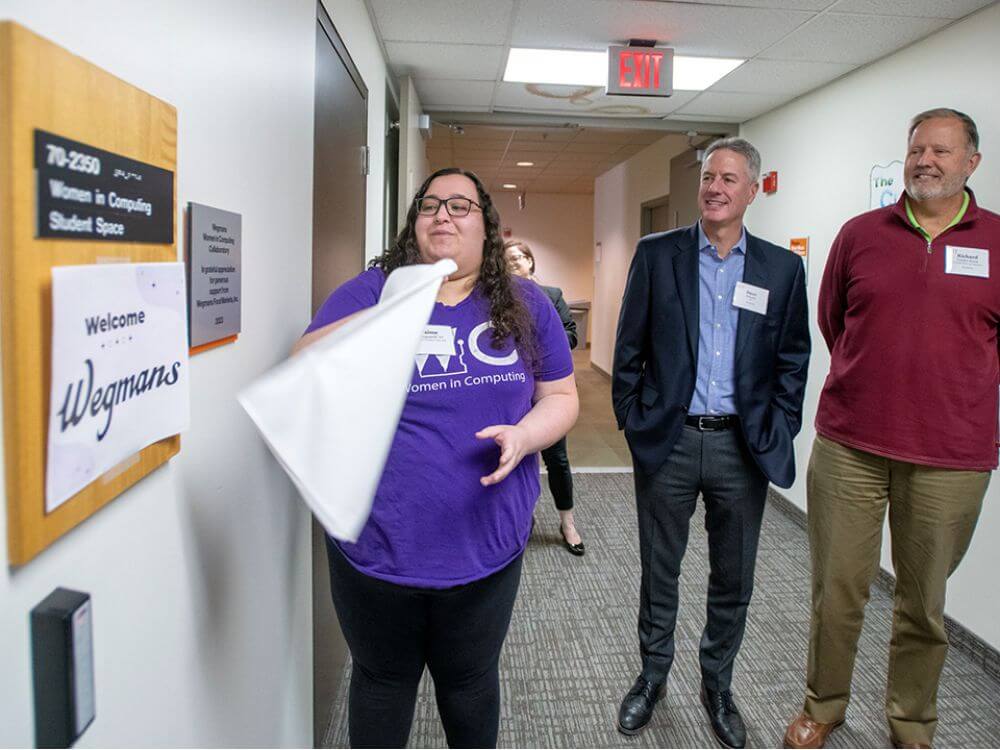 Three people standing looking at new sign by door for Women in Computing Collaboratory.