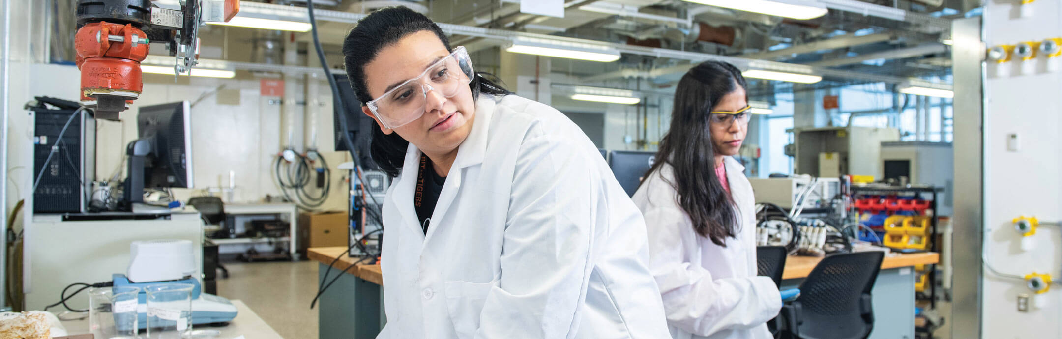 Two female students in white lab coats working in a lab