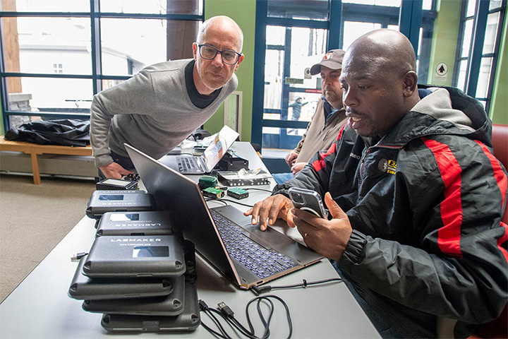 3 men standing around a laptop computer.