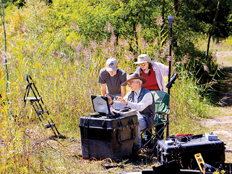3 researchers outside in an outdoor setting, using measuring instruments.