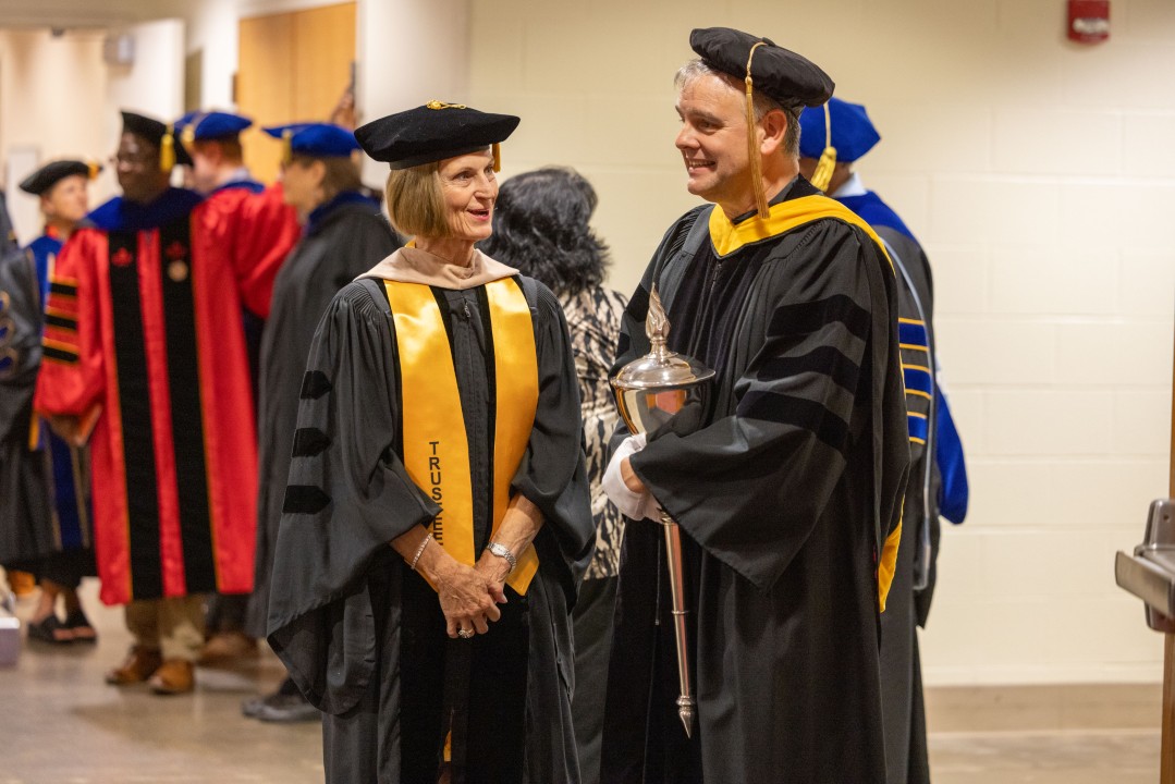 A trustee in gold-trimmed regalia chats with the mace bearer backstage before the procession.