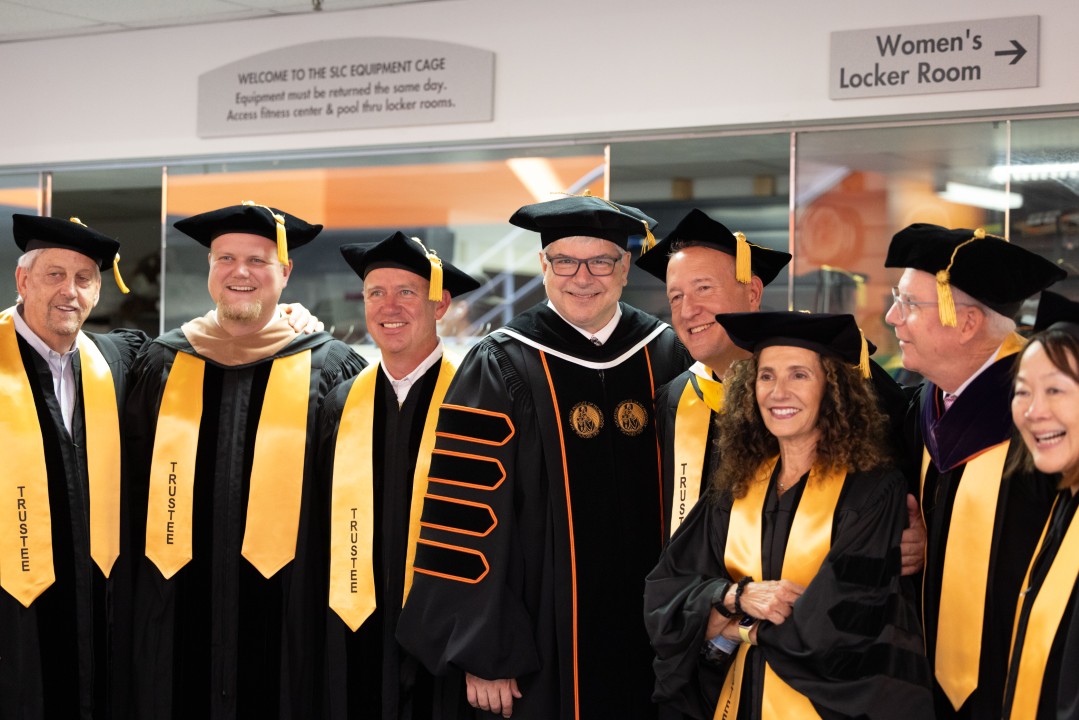 Trustees and the president in regalia gather together smiling for a group photo backstage.