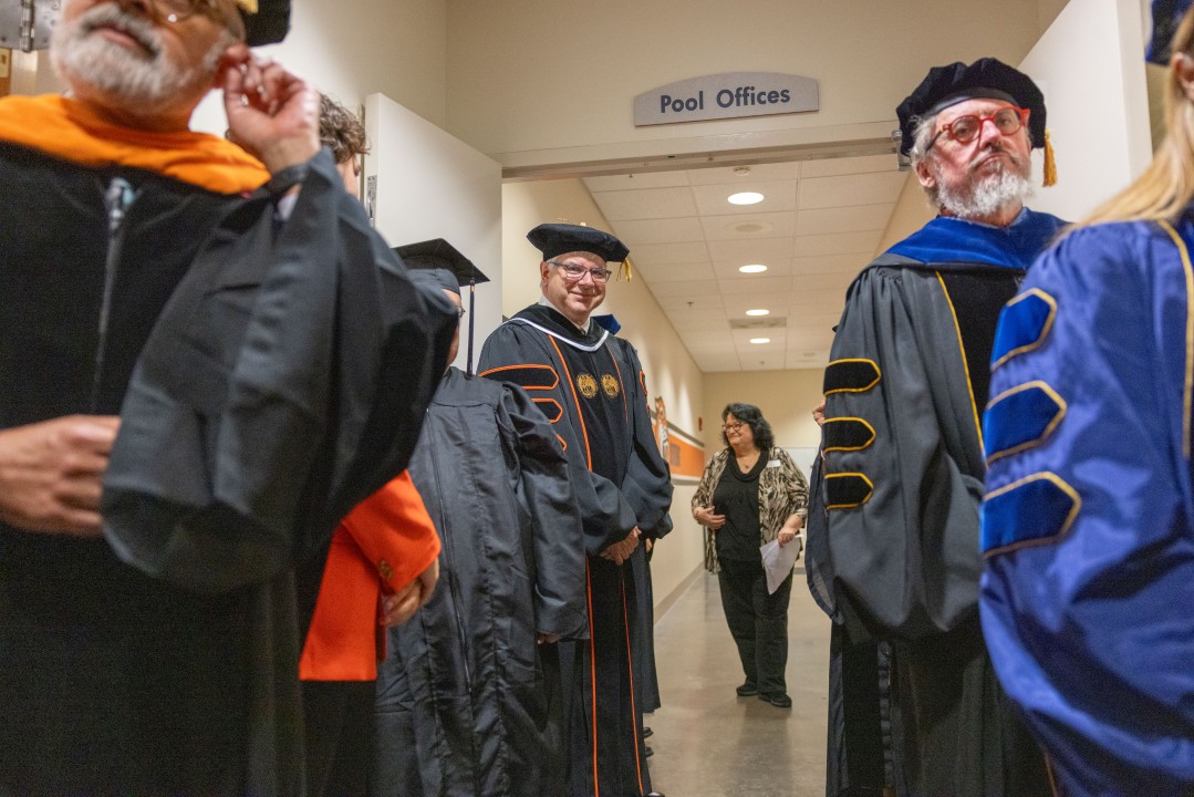 R I T President Sanders wearing academic regalia waits in a hallway as other professors line up before the procession.