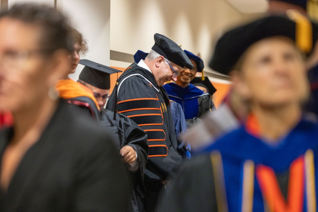R I T President Sanders wearing academic regalia waits in a hallway as other professors in caps and gowns line up in a hallway before the academic procession.