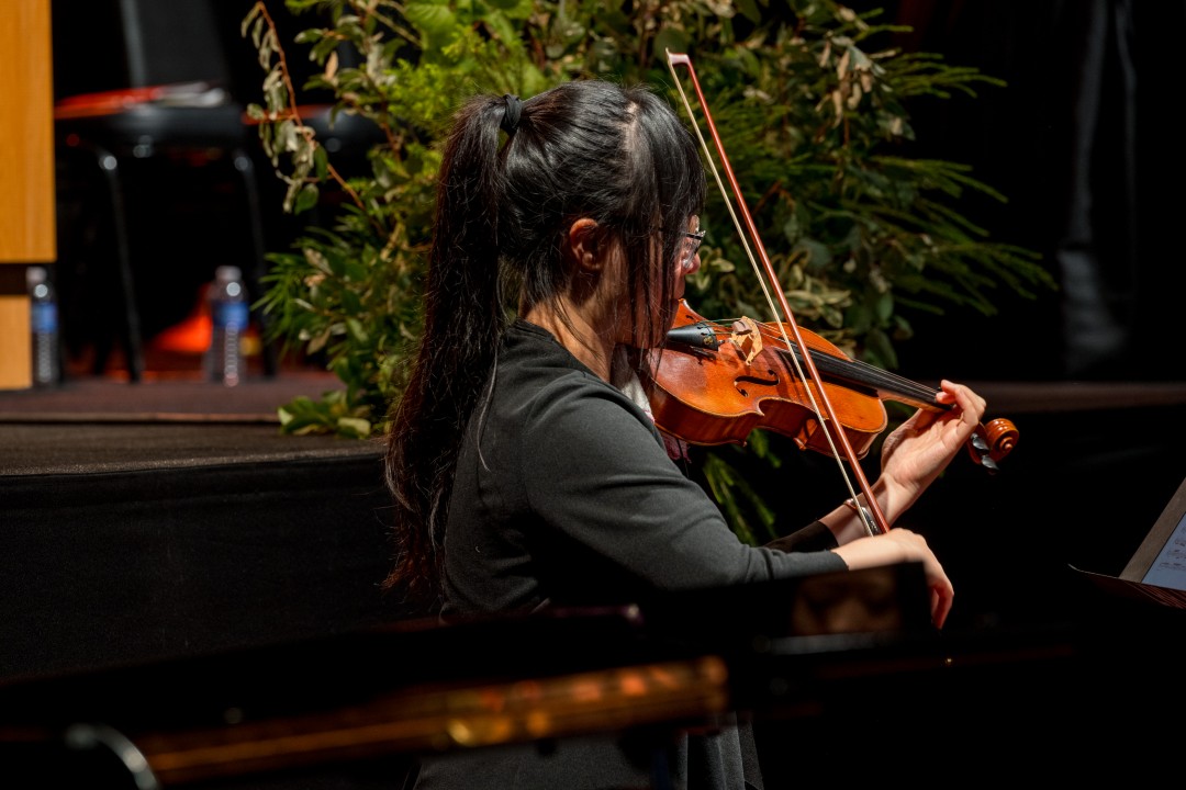 A violinist performs on stage during the inauguration with greenery in the background.