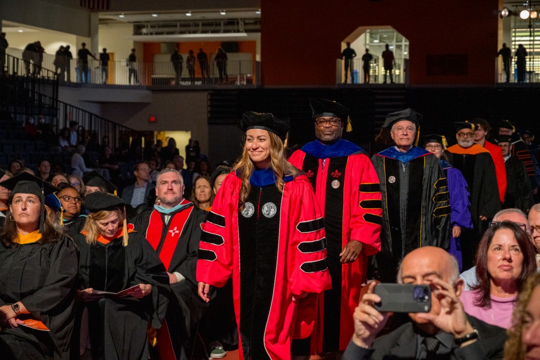 Faculty in academic regalia process down the aisle during an inauguration ceremony as attendees watch.